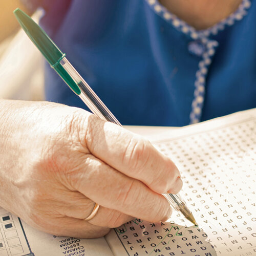 En äldre kvinna med penna i handen löser ett ordpussel.