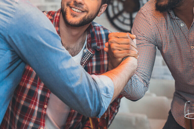 Två män tar varandra i handen medan en tredje man ler mot en av dem.