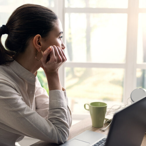 En person sitter med huvudet i handen och blickar ut genom fönstret.