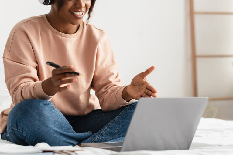 En person sitter på sin säng och pratar engagerat med någon i ett digitalt möte.